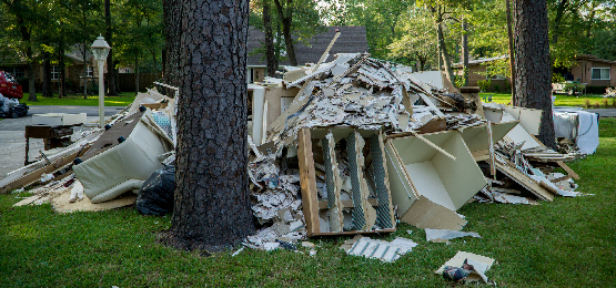 Large pile of flood-damaged household items collected on a front lawn for trash removal.